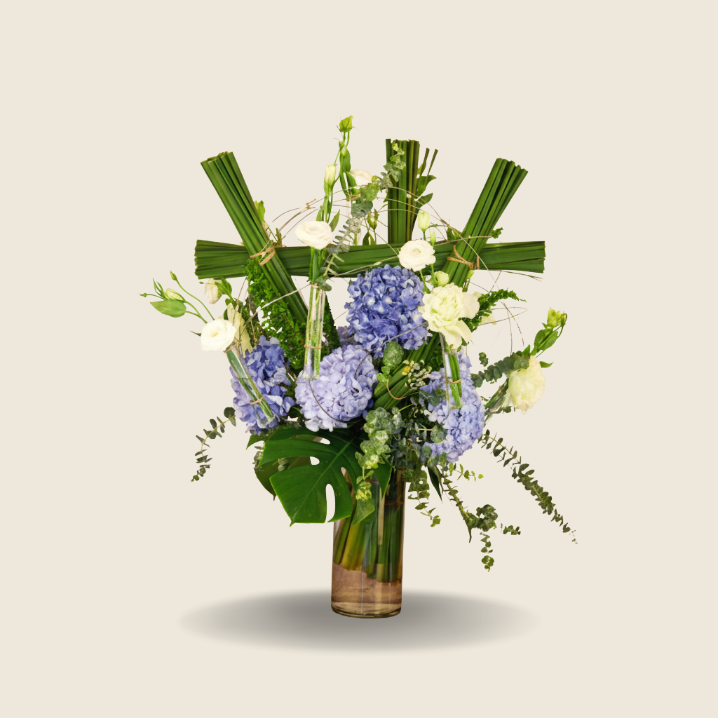 Tall glass vase with blue hydrangeas, white eustoma, and tropical greens